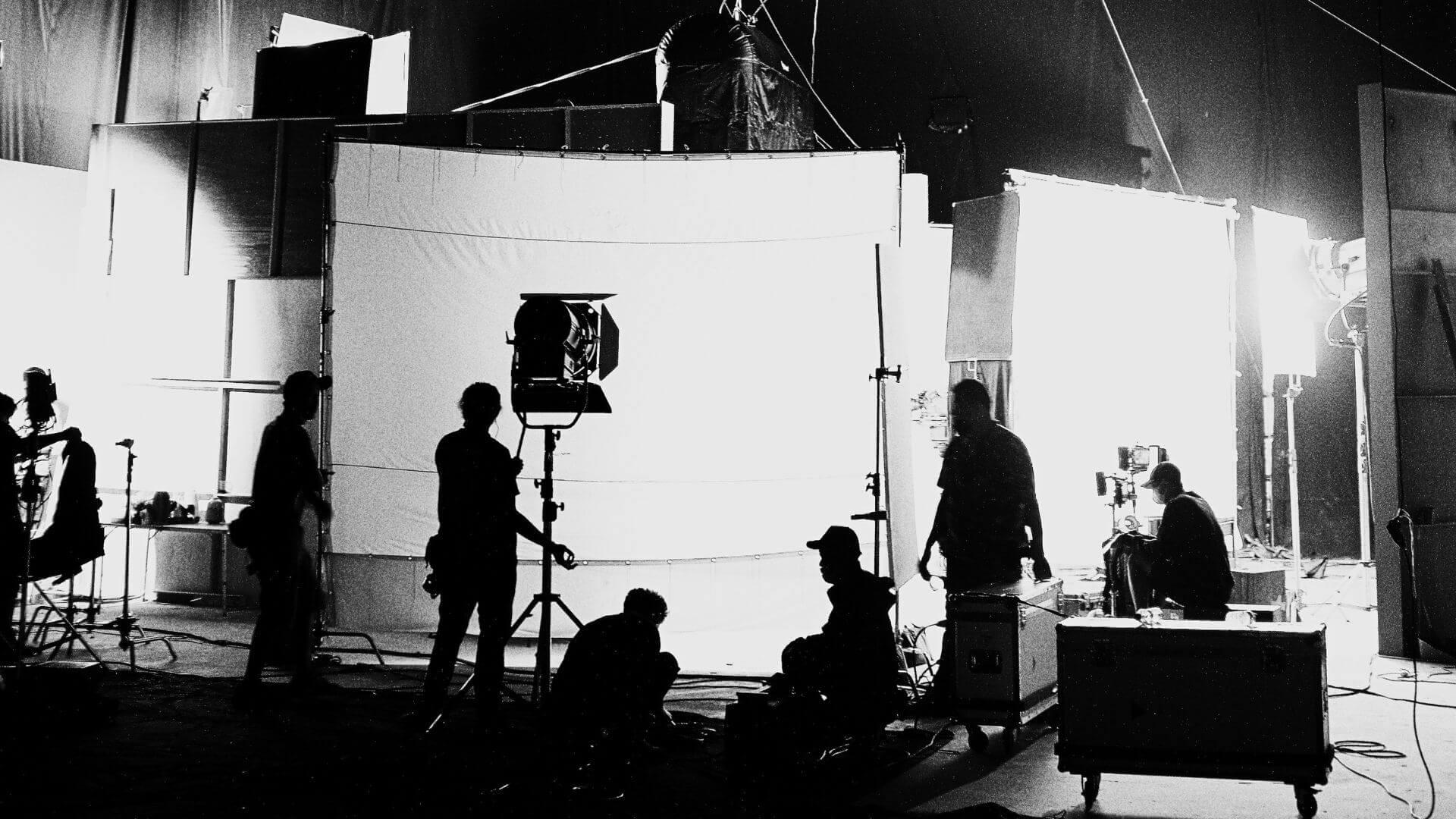 produzione-set-cinematografico | Jessica Lima Vista ad ampio raggio di un teatrale di posa in bianco e nero con luci di scena e troupe al lavoro