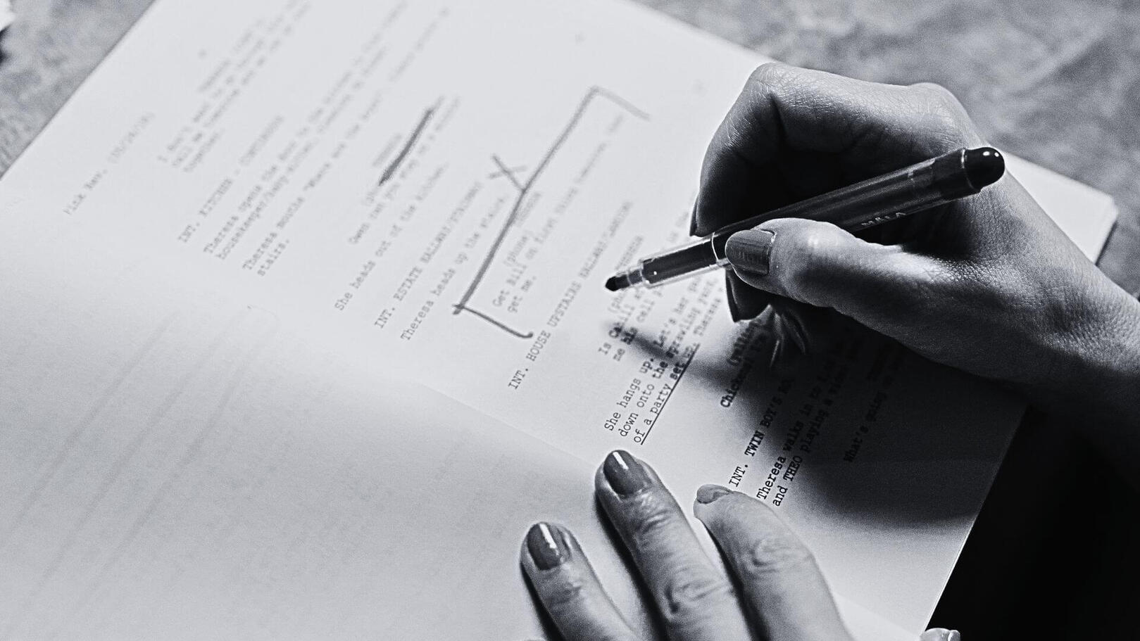 Narrative Consulting and Script Editorial - Jessica Lima Dettaglio in bianco e nero di una mano che evidenzia e annota correzioni con una penna su una pagina di sceneggiatura stampata.
